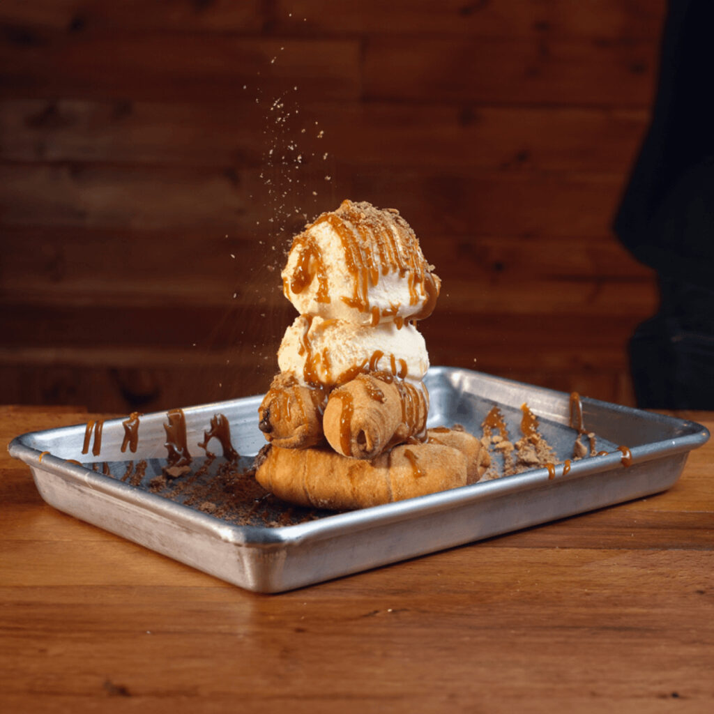 Tequeños rellenos de nutella, sobre una bola de helado de vainilla, bañado en dulce de leche y galletas trituradas en Madrid