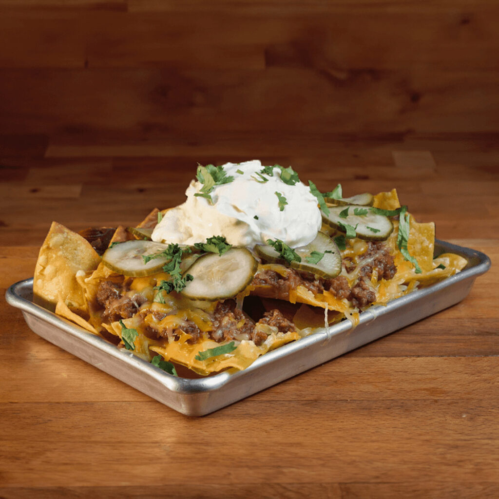 Nachos Carne al estilo Sloppy Joe de ternera picada, cocinada por horas con tomate y especias, mix de quesos americanos, crema agria y pepinillos en Madrid