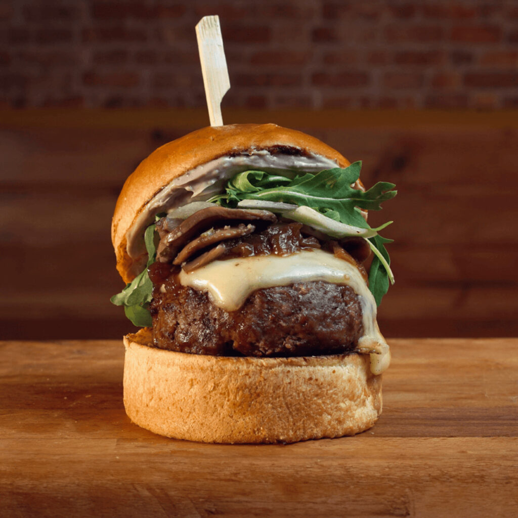 Hamburguesa de carne a la brasa, queso Monterrey Jack, champiñones marinados y salteados con cebolla, mayonesa de Trufa, láminas de parmiggiano y rúcula en Madrid